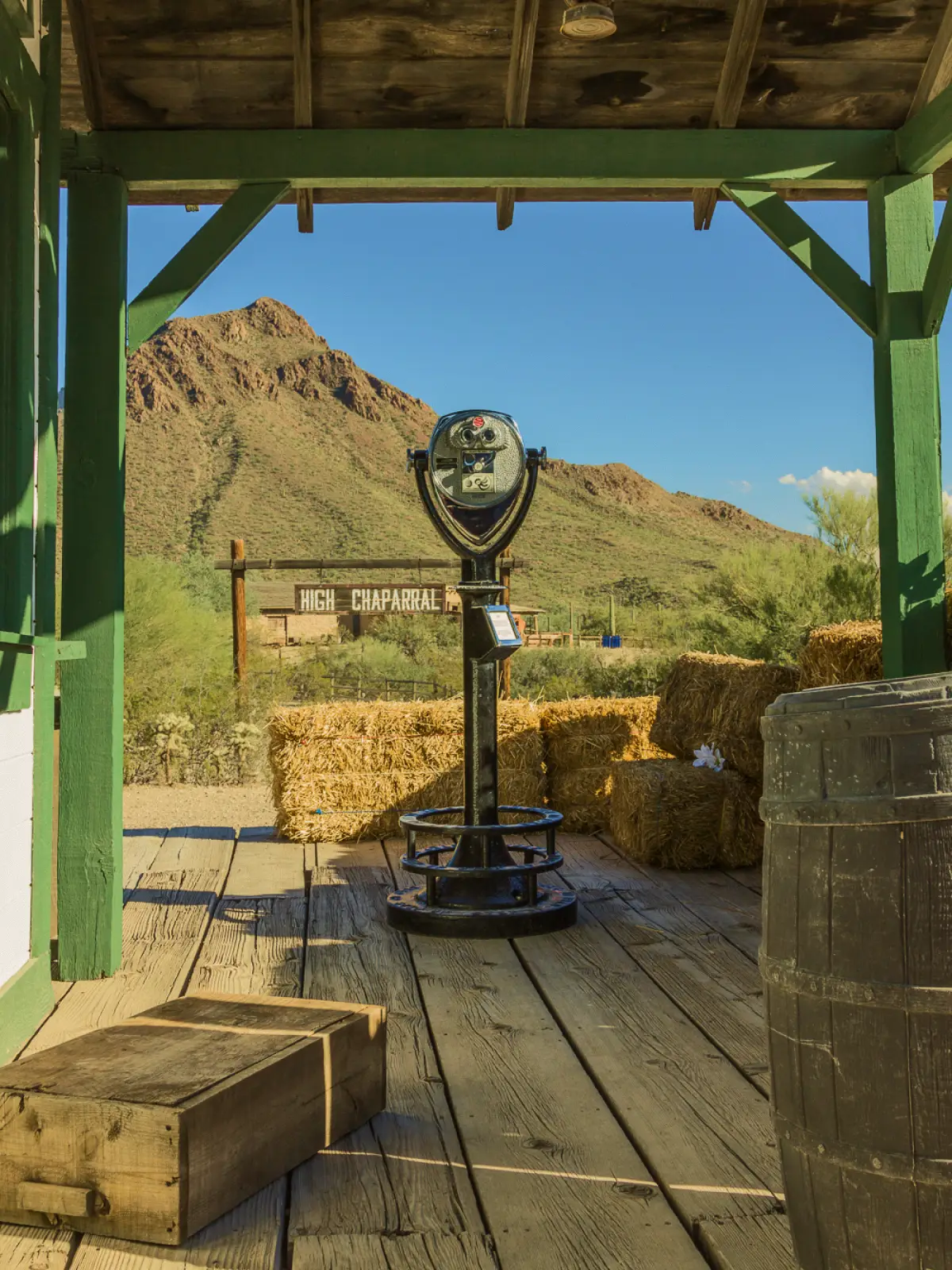 A Tower Optical coin-operated binocular viewer installed at a rustic desert overlook with hay bales, wooden beams, and mountain scenery in the background