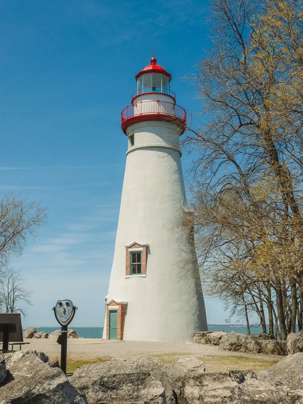 A Tower Optical coin-operated binocular viewer near a historic white lighthouse overlooking the coast