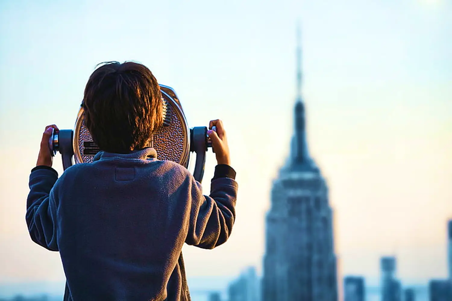 A child looking through an optical viewer over the New York City skyline