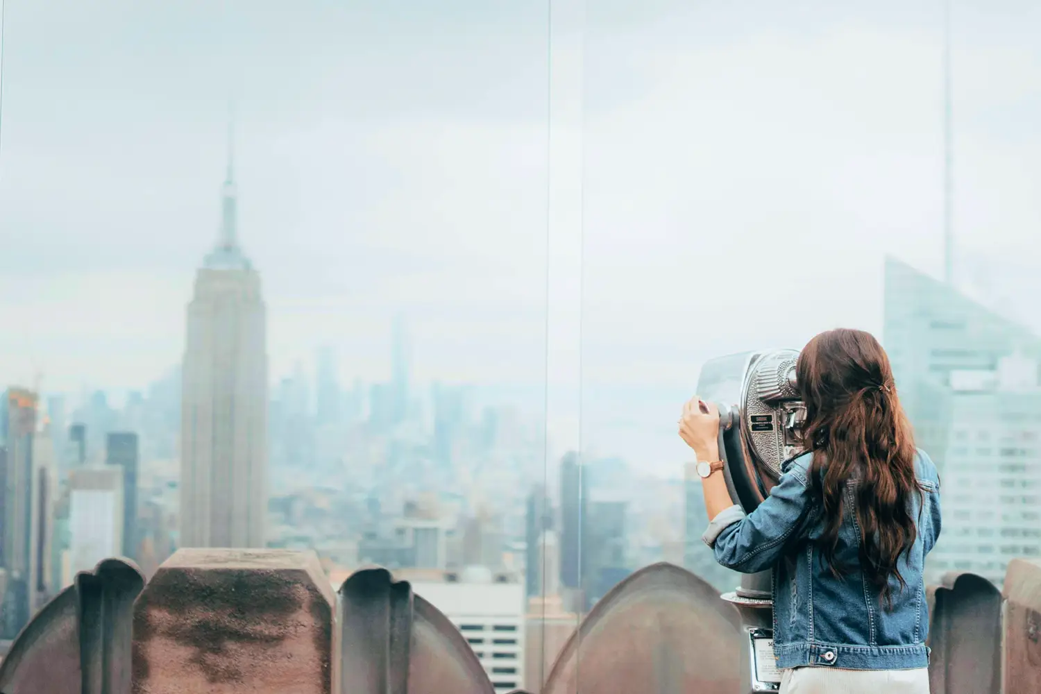 A woman uses a Tower Optical coin-operated binocular viewer to look at the New York City skyline and the Empire State Building from an observation deck