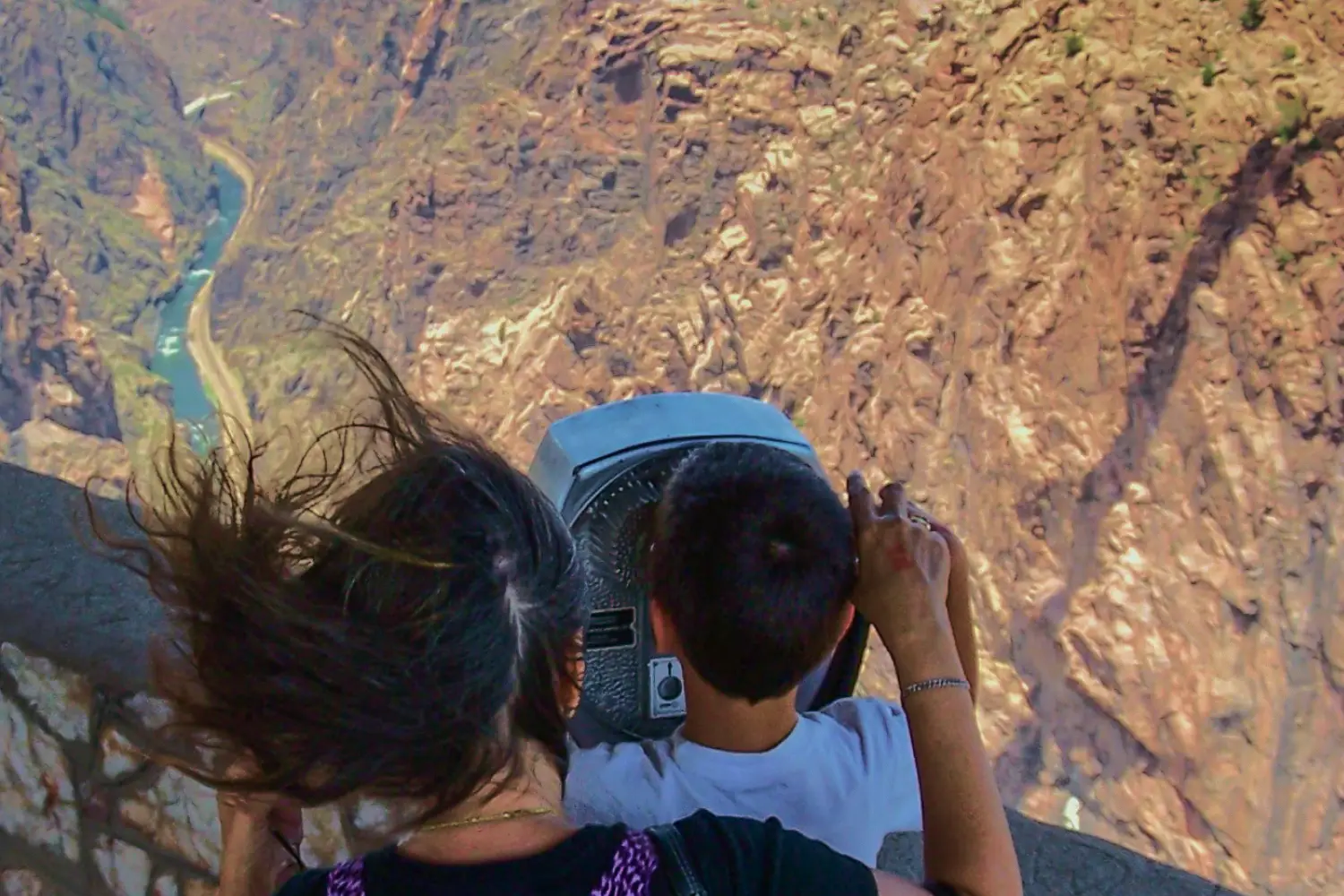 Two people use a Tower Optical coin-operated binocular viewer to look out over a deep canyon with a winding river below