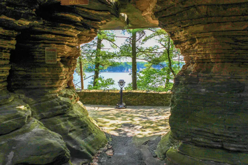 A Tower Optical Coin-Operated Binocular Viewers framed by a natural rock archway overlooking a scenic lake and forest.