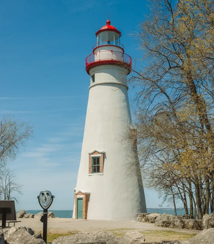 A Tower Optical coin-operated binocular viewer near a historic white lighthouse overlooking the coast.